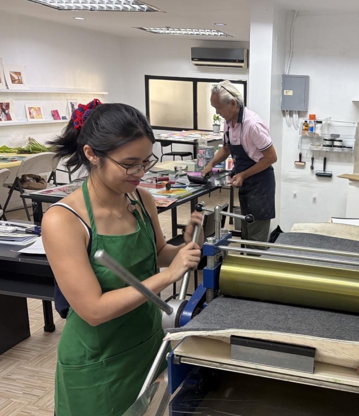 A student runs a plate through the etching press while Benjie inks behind